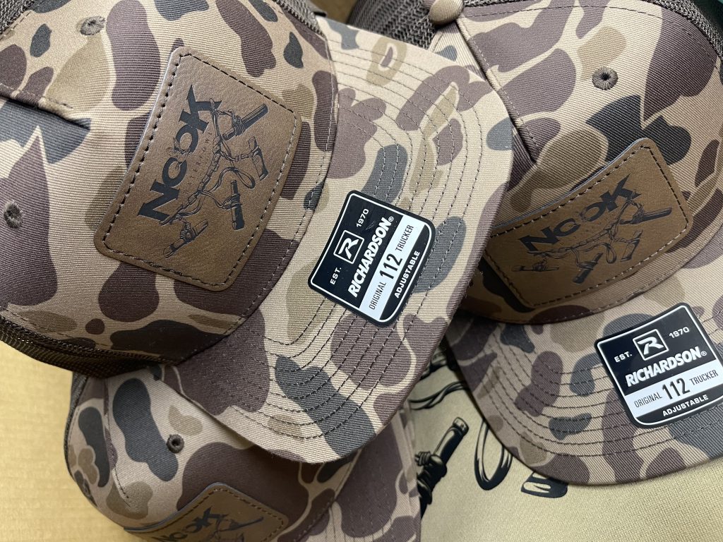Camo trucker hats with brown leatherette patches engraved with the Nook Waterfowl logo