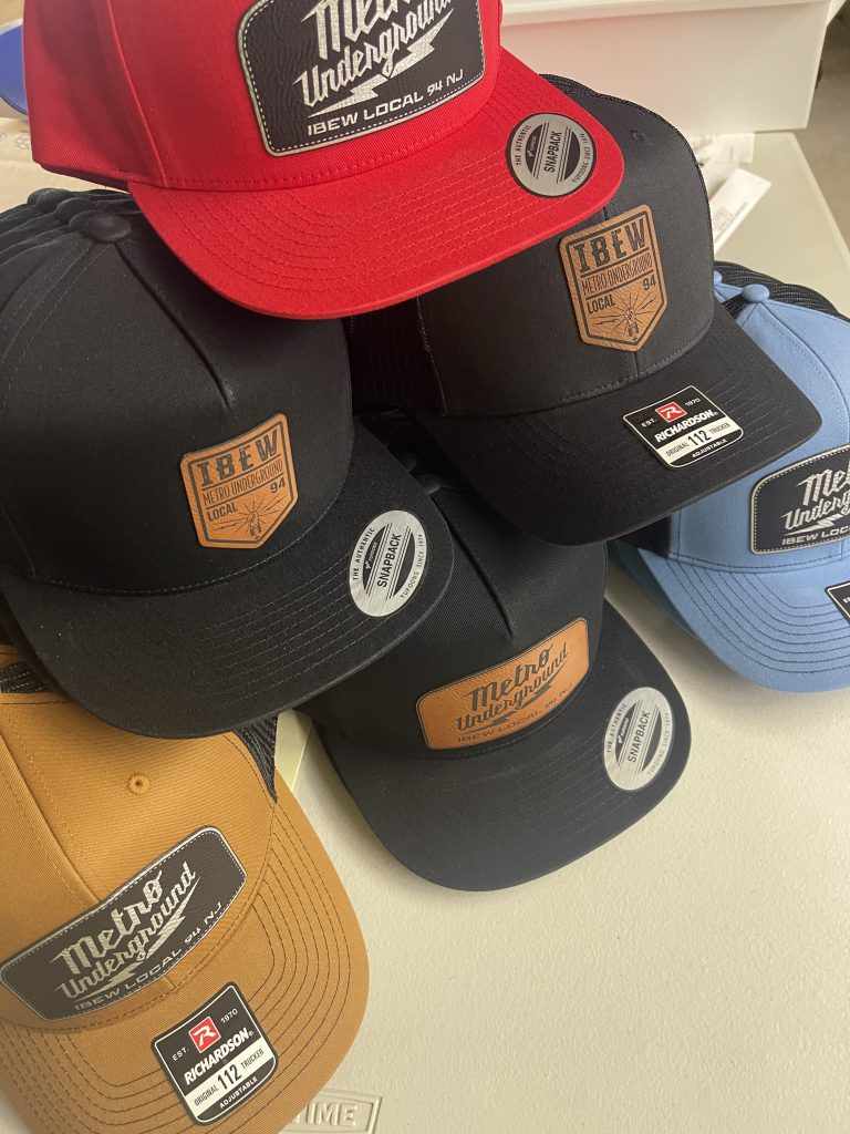 Black, red, blue and gold trucker hats with engraved leatherette IBEW Local 94 and Metro Underground patches