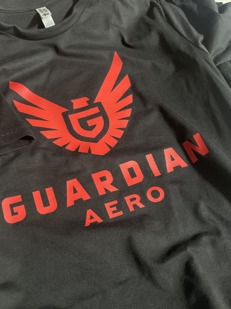 Black tee printed in red with the Guardian Aero winged-G logo and wordmark