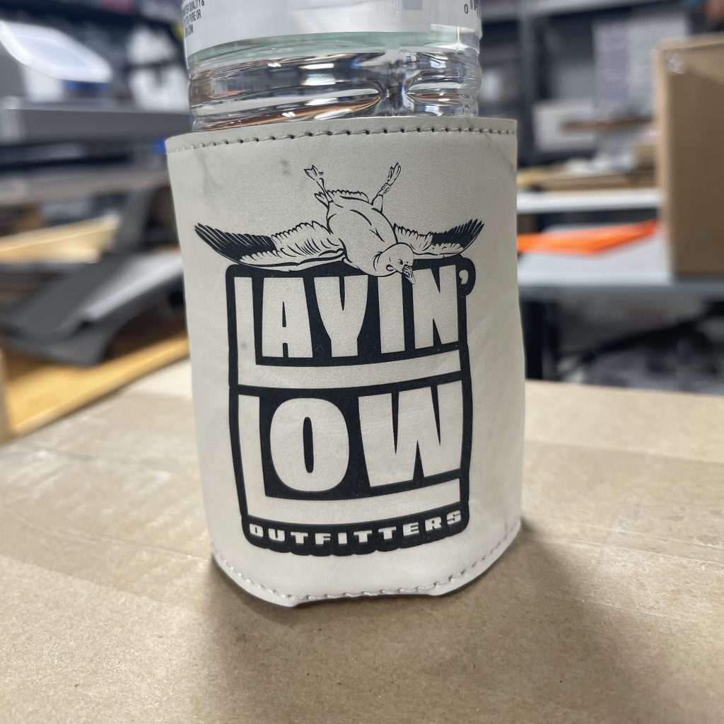 White leatherette can cooler engraved with the Layin' Low Outfitters logo, on a bottle