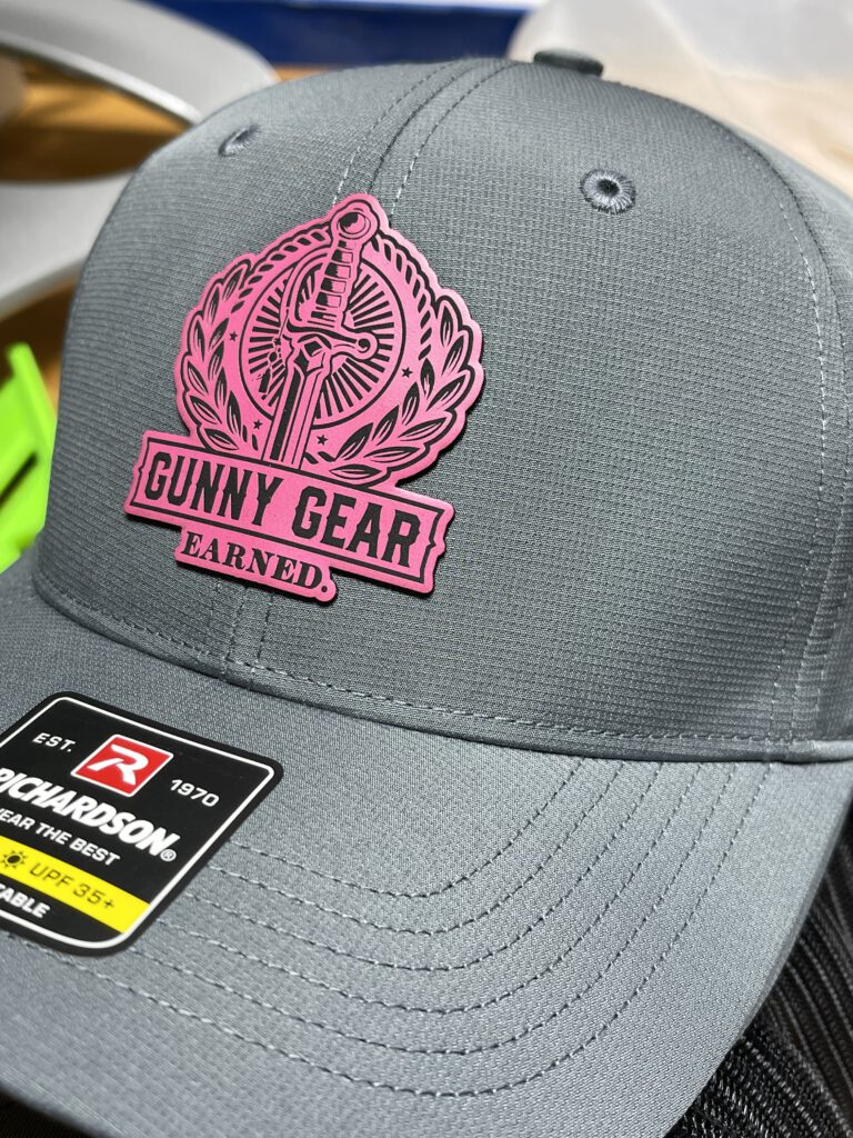 Charcoal hat with a pink Gunny Gear patch: a sword in a laurel wreath above Gunny Gear Earned