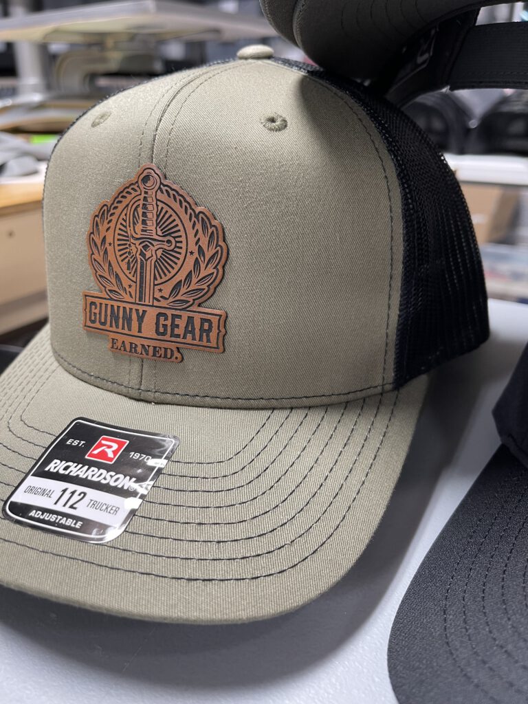 Khaki and black trucker hat with a brown leatherette Gunny Gear patch