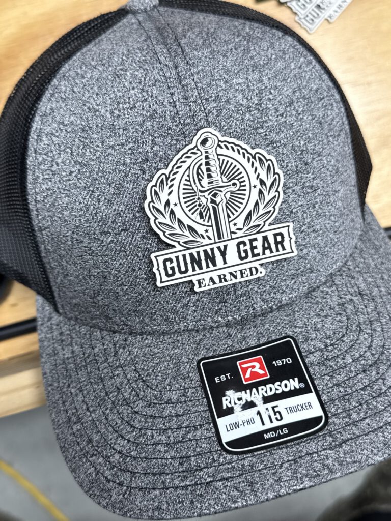 Heather gray trucker hat with a white and black Gunny Gear patch