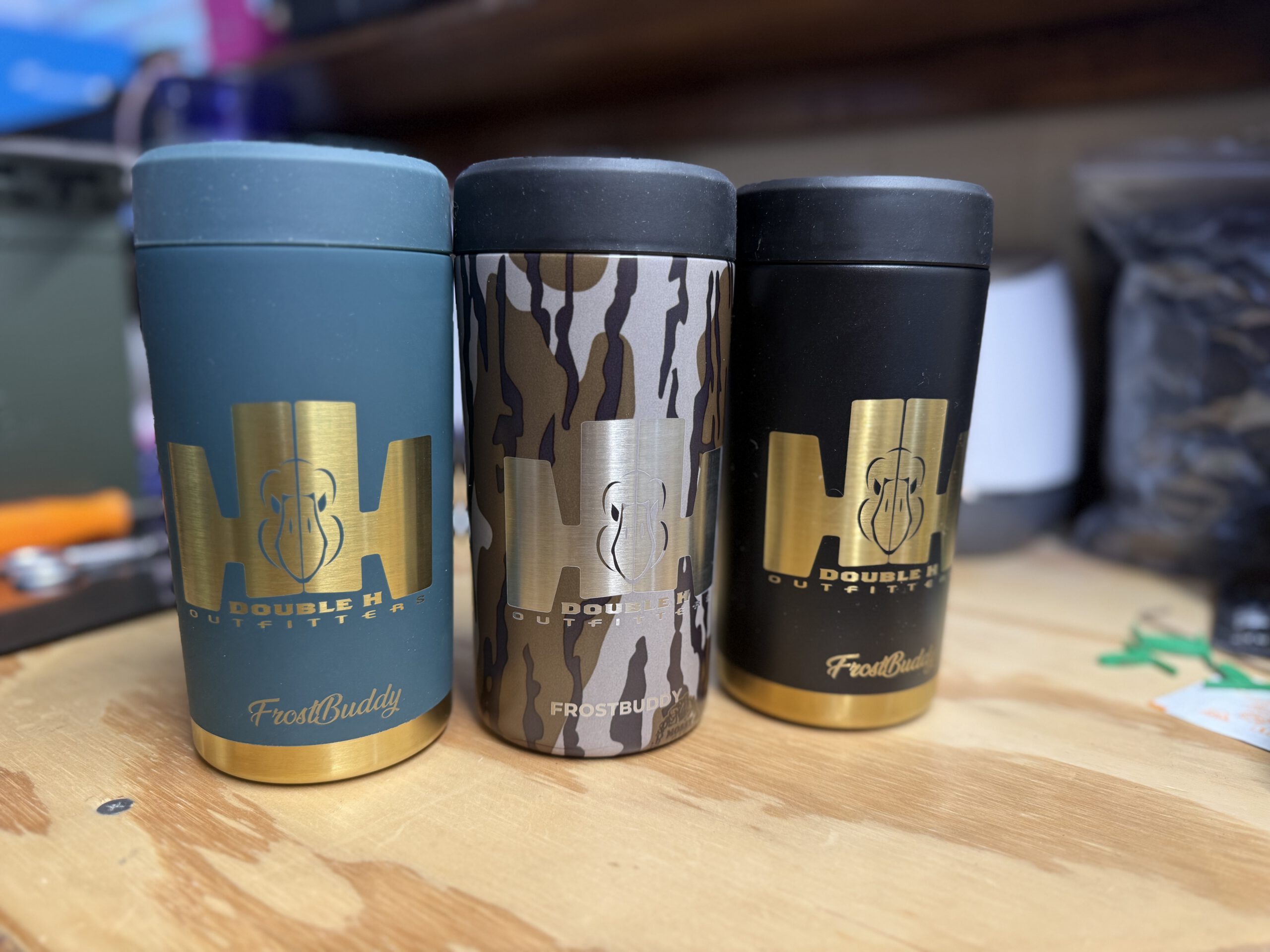 Three can coolers in blue, camo and black, engraved in gold with the Double H Outfitters HH mark