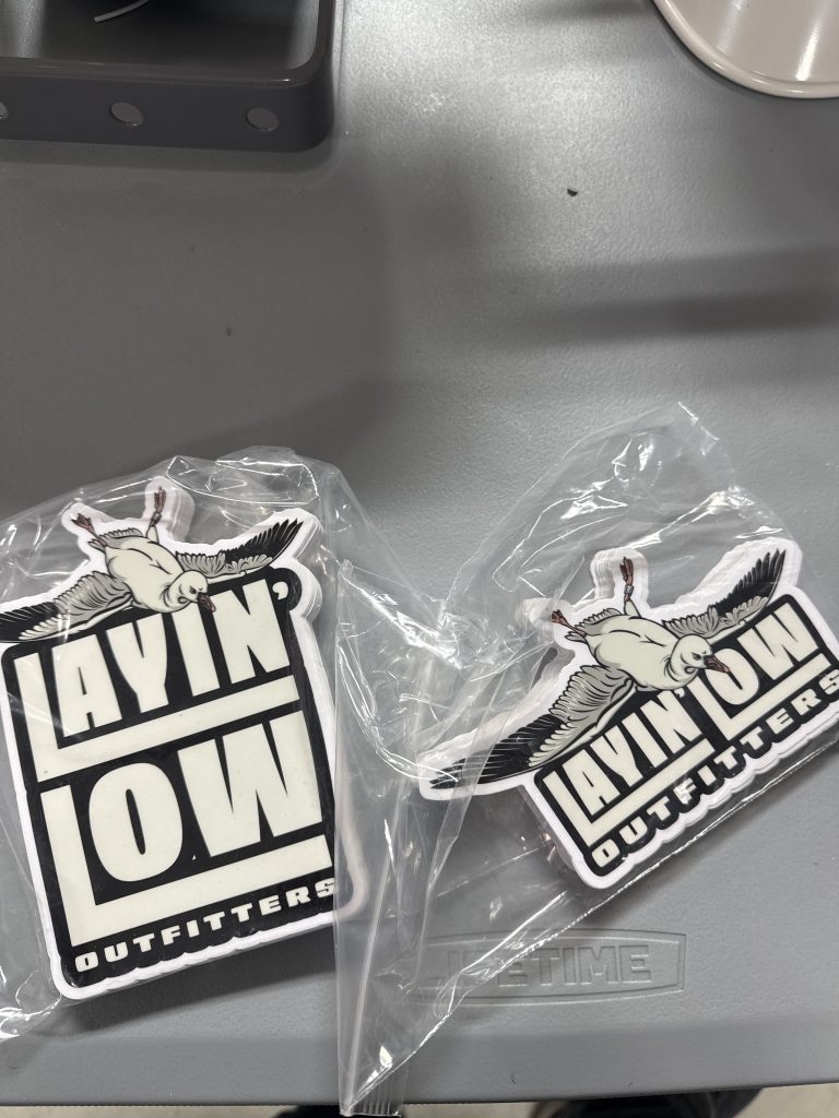 Two die-cut Layin' Low Outfitters stickers with the snow goose logo, in clear sleeves