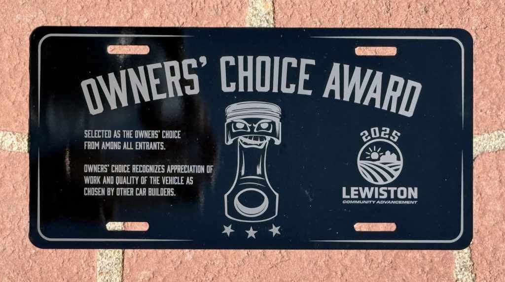 Black aluminum license plate engraved as an Owners' Choice Award, with a piston illustration and the 2025 Lewiston Community Advancement logo