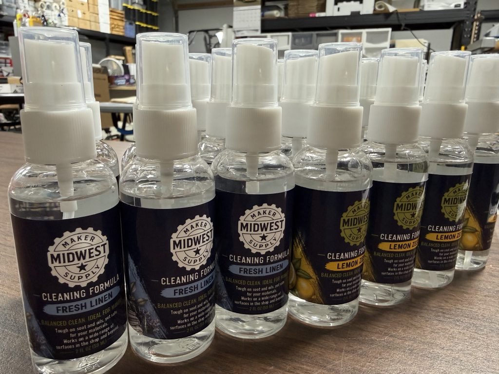 Rows of spray bottles labeled Midwest Maker Supply Cleaning Formula, in Fresh Linen and Lemon Zest scents