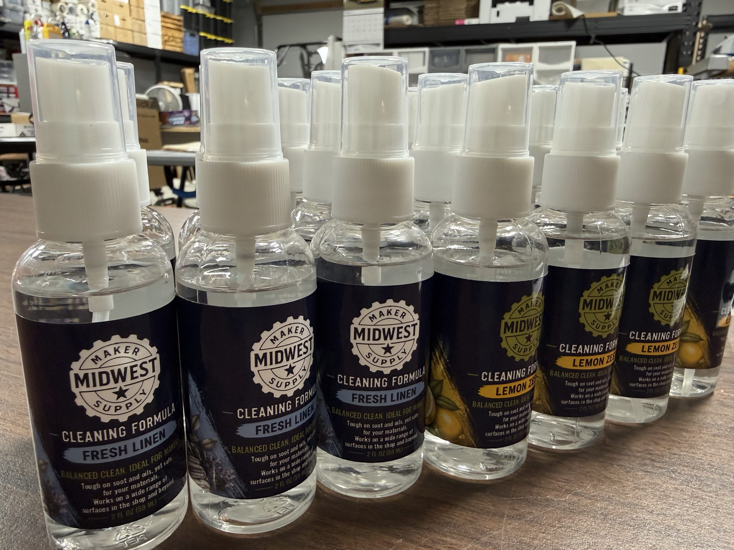 Rows of spray bottles labeled Midwest Maker Supply Cleaning Formula, in Fresh Linen and Lemon Zest scents