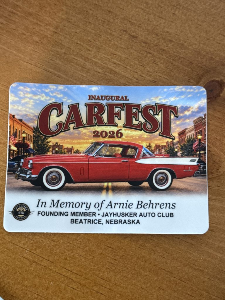 Inaugural Carfest 2026 sticker with a red classic car on a downtown street at sunset, in memory of Arnie Behrens, founding member of the JayHusker Auto Club, Beatrice, Nebraska
