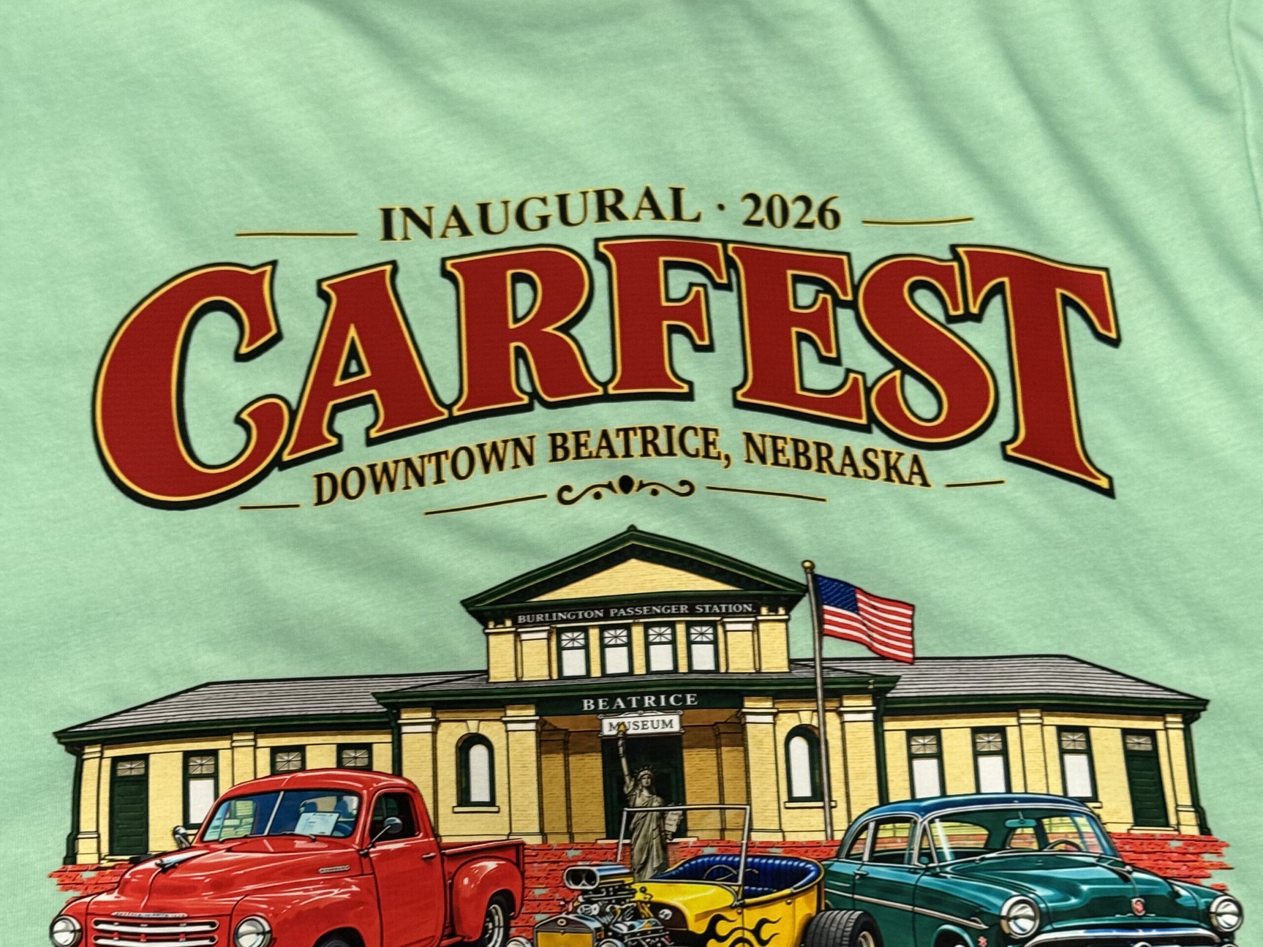 Mint green shirt printed with the Inaugural 2026 Carfest design: classic cars in front of the Burlington Passenger Station in downtown Beatrice