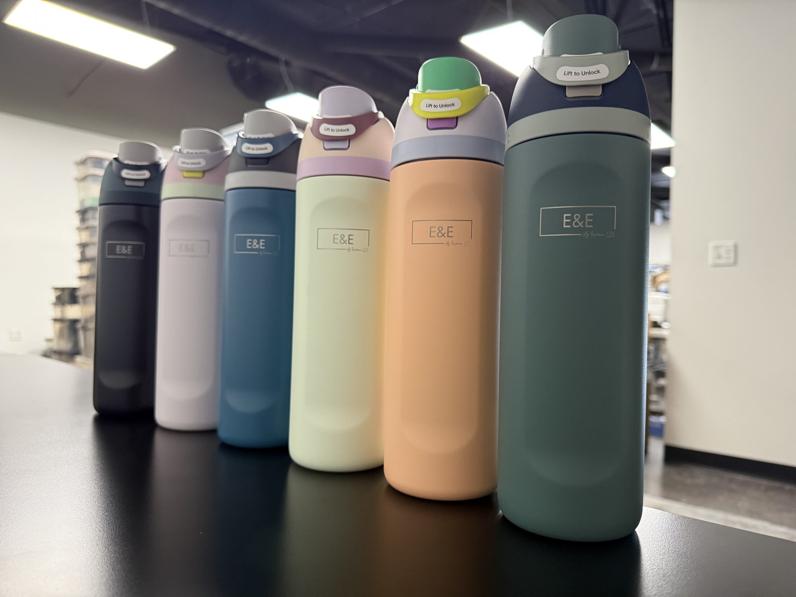Six insulated water bottles in assorted colors lined up on a shop counter, each engraved with the E&E Ag Insurance logo