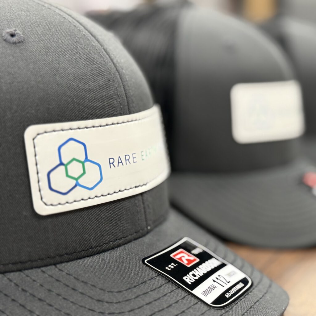 A row of charcoal trucker hats with white Rare Earth Salts patches, the nearest in focus