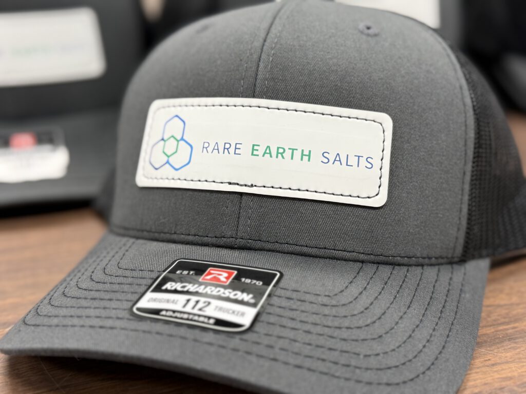 Charcoal and black trucker hat with a white patch printed with the Rare Earth Salts logo
