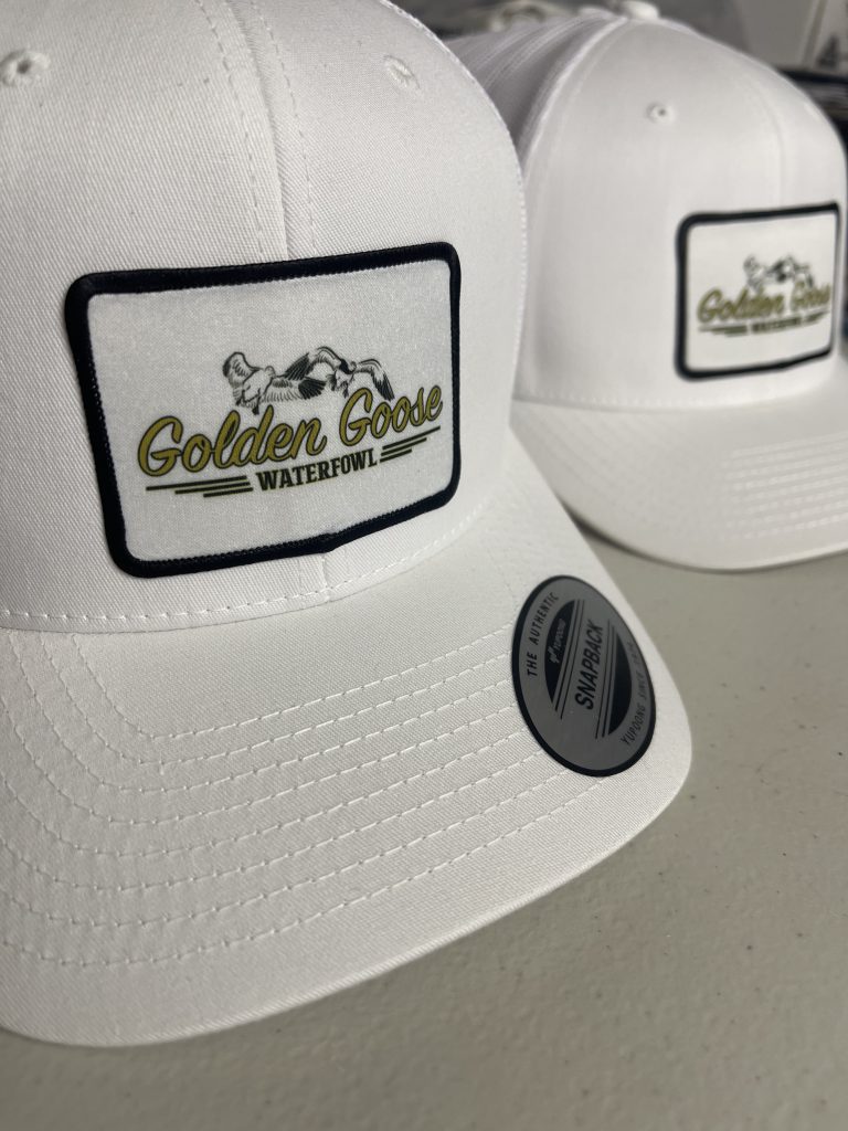 White hats with full-color Golden Goose Waterfowl patches edged in black stitching
