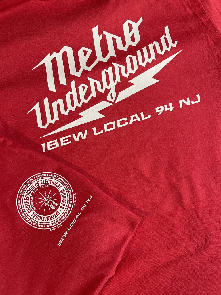 Red tee printed in white with Metro Underground script lettering, a lightning bolt and IBEW Local 94 NJ, with the union seal on the sleeve