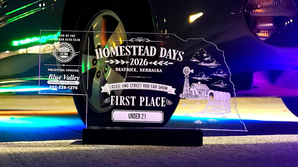 The Nebraska-shaped Homestead Days First Place award in front of a car lit by colored underglow