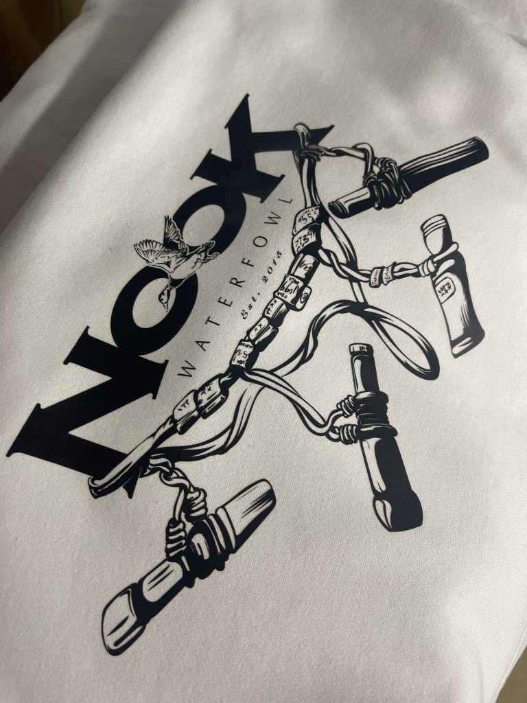 Cream tee printed in black with the Nook Waterfowl logo above a lanyard of waterfowl calls