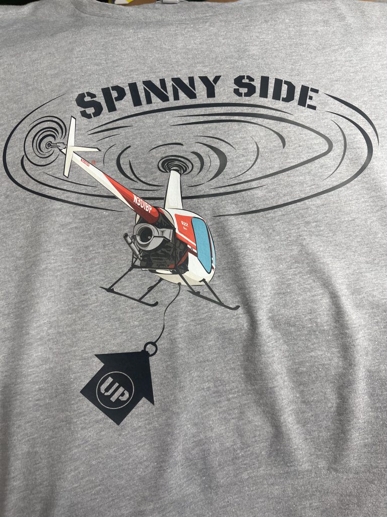 Gray tee printed with the Spinny Side Up design: a helicopter in a spiral of rotor wash, towing an Up sign